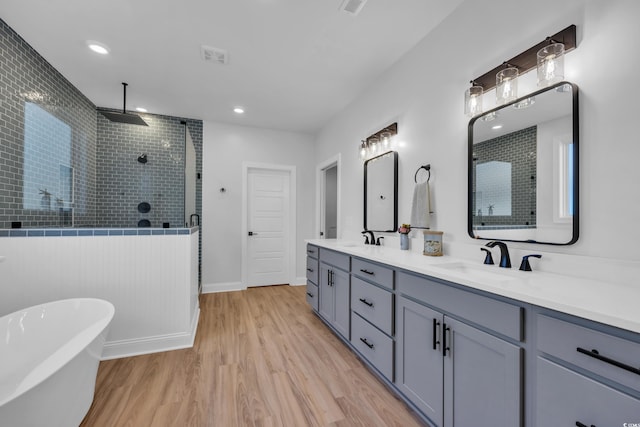 full bathroom with double vanity, tiled shower, a sink, and wood finished floors