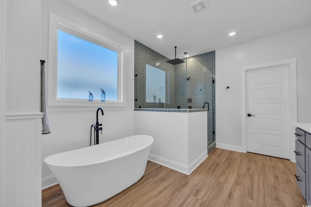 full bath featuring a freestanding bath, wainscoting, wood finished floors, visible vents, and a stall shower