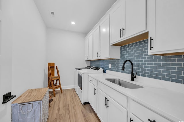 kitchen featuring washing machine and clothes dryer, white cabinets, a sink, light wood finished floors, and decorative backsplash
