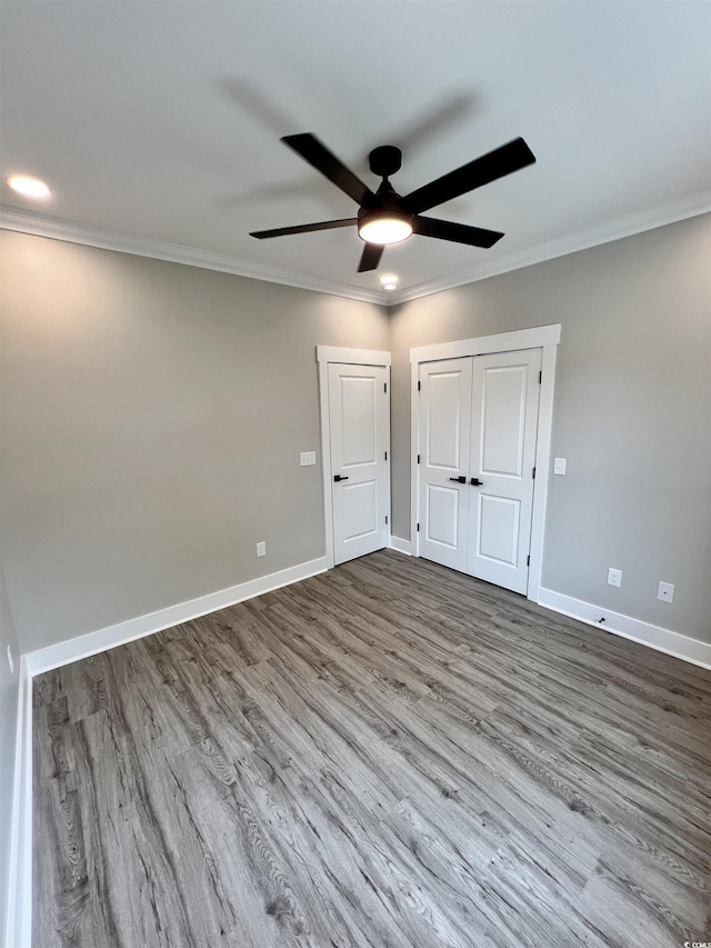 unfurnished bedroom with a closet, dark wood-type flooring, baseboards, ceiling fan, and ornamental molding