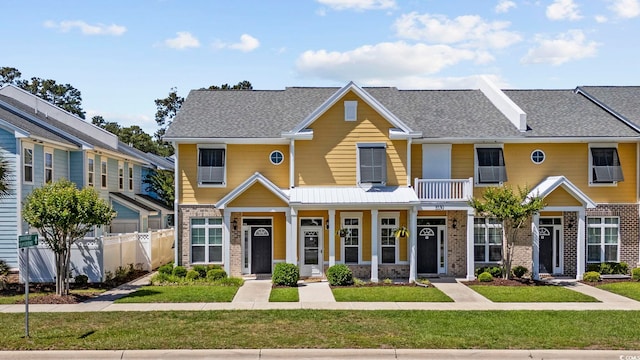 townhome / multi-family property with covered porch, roof with shingles, brick siding, fence, and a front lawn