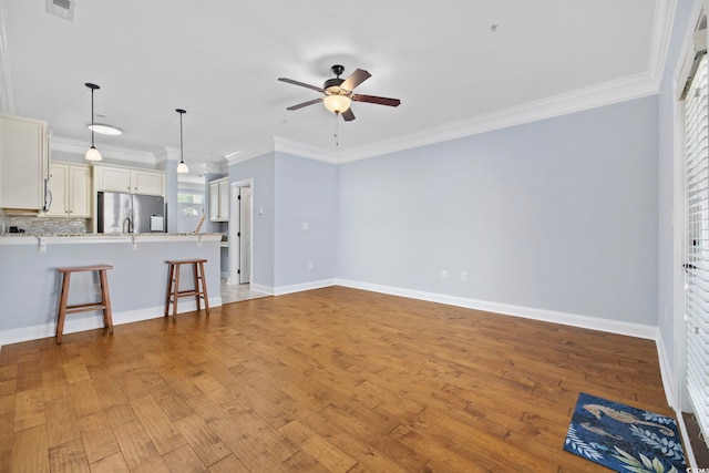 unfurnished living room with crown molding, ceiling fan, baseboards, light wood-type flooring, and visible vents