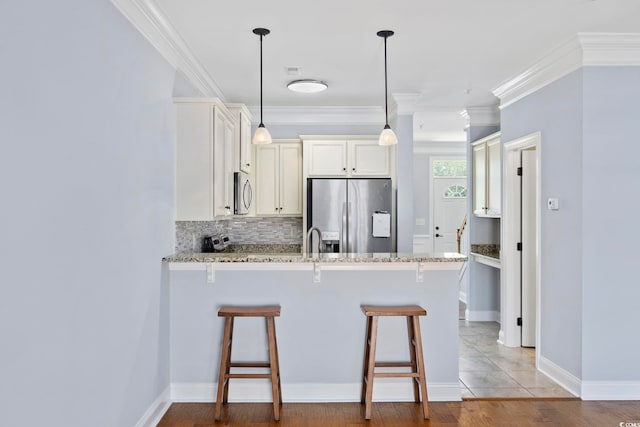 kitchen featuring light stone counters, a kitchen breakfast bar, stainless steel appliances, a peninsula, and decorative backsplash