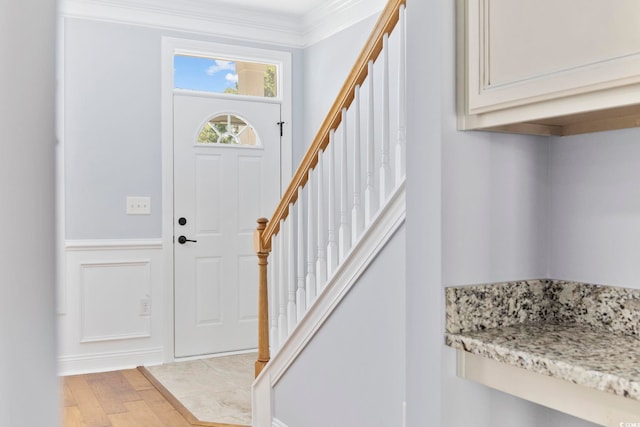 foyer featuring light wood-type flooring, ornamental molding, and stairway