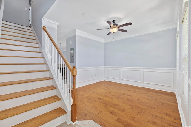 stairway with crown molding, a ceiling fan, wainscoting, and electric panel