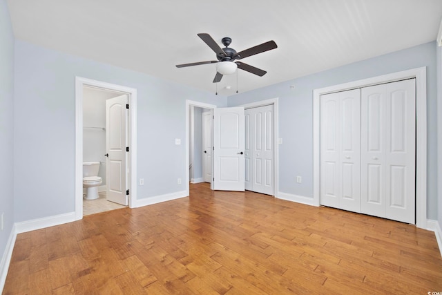 unfurnished bedroom featuring baseboards, multiple closets, light wood-style flooring, and ensuite bathroom