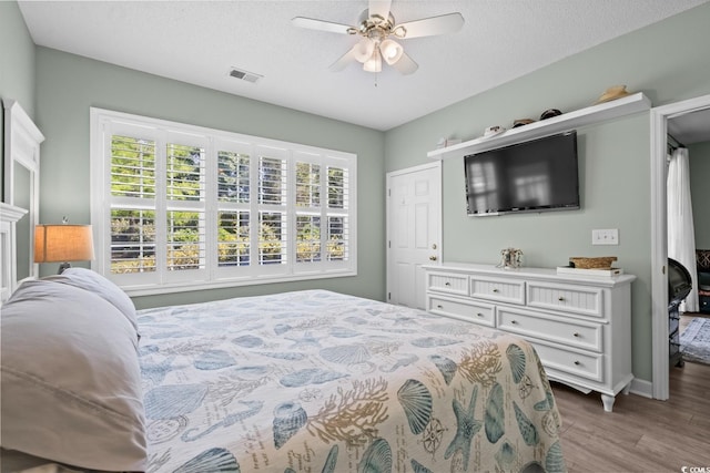 bedroom featuring a ceiling fan, a textured ceiling, visible vents, and wood finished floors