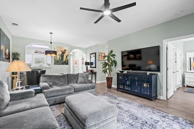 living room featuring ceiling fan, a textured ceiling, visible vents, arched walkways, and wood finished floors