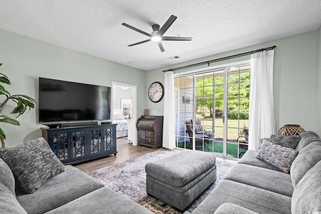 living room featuring ceiling fan, a textured ceiling, visible vents, and wood finished floors