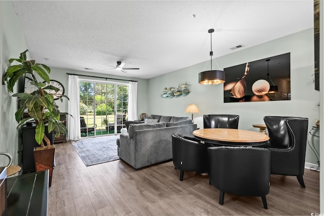 living room with a textured ceiling, ceiling fan, wood finished floors, and visible vents