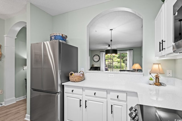 kitchen with arched walkways, white cabinets, freestanding refrigerator, and wood finished floors