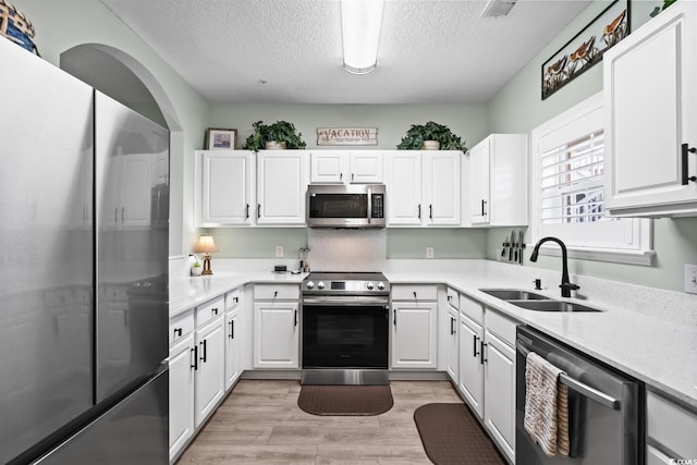 kitchen featuring stainless steel appliances, a textured ceiling, white cabinetry, and a sink