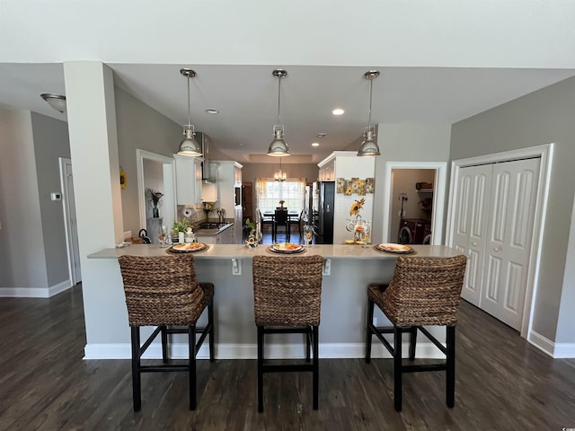 kitchen featuring freestanding refrigerator, a peninsula, white cabinetry, and dark wood-type flooring