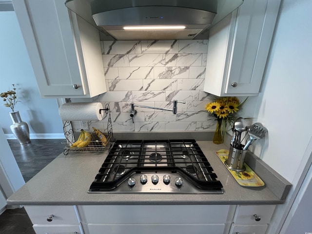 kitchen featuring stainless steel gas cooktop, white cabinets, under cabinet range hood, and tasteful backsplash