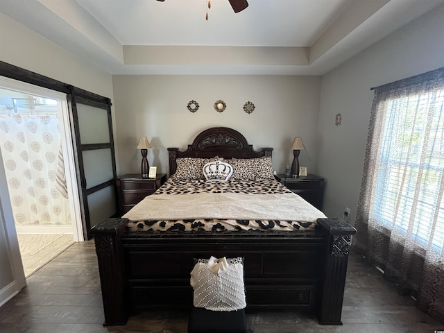 bedroom with a raised ceiling, dark wood-style flooring, ceiling fan, and ensuite bath