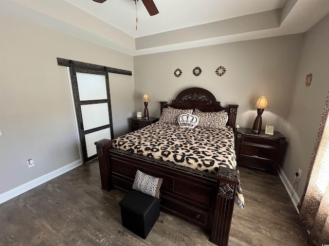 bedroom featuring ceiling fan, a barn door, baseboards, wood finished floors, and a tray ceiling