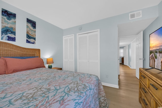 bedroom with visible vents, baseboards, wood finished floors, and two closets
