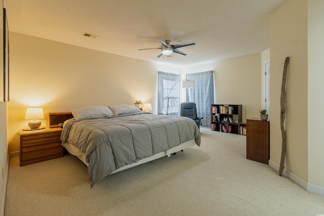 bedroom with a textured ceiling, ceiling fan, visible vents, and light carpet