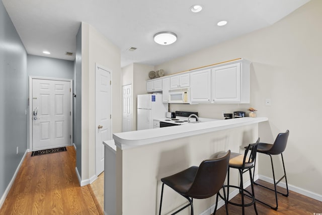 kitchen with white cabinets, a breakfast bar area, white appliances, and light wood-style flooring