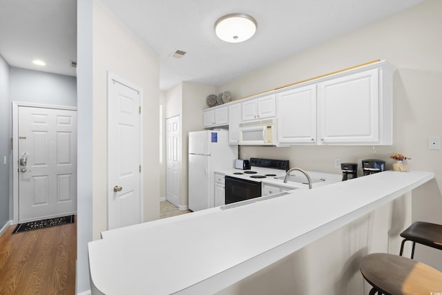 kitchen with visible vents, white appliances, baseboards, a kitchen bar, and light wood-type flooring
