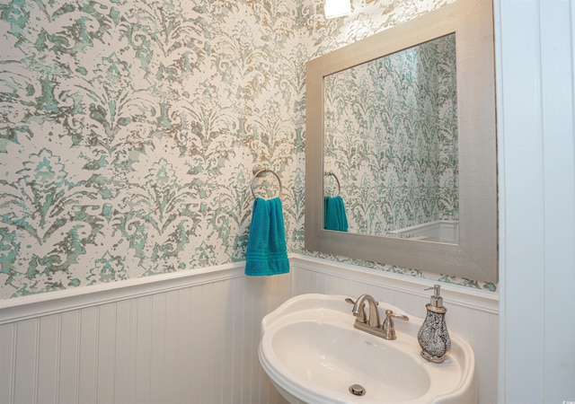 bathroom with a sink, a wainscoted wall, and wallpapered walls