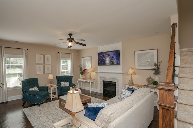 living area with a glass covered fireplace, baseboards, ceiling fan, stairway, and dark wood-type flooring