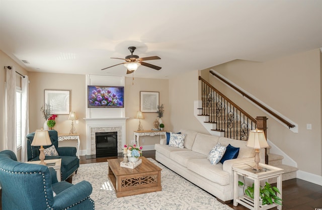 living area featuring a premium fireplace, ceiling fan, dark wood finished floors, and stairs