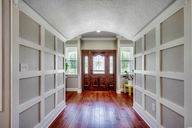 entrance foyer featuring crown molding, a textured ceiling, dark wood finished floors, and arched walkways