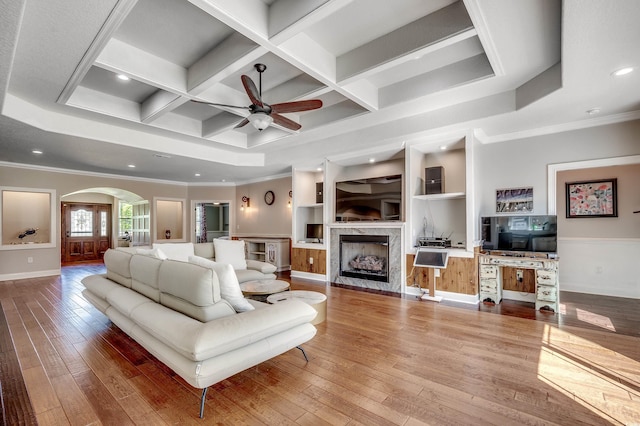 living room featuring wood-type flooring, a ceiling fan, crown molding, baseboards, and arched walkways