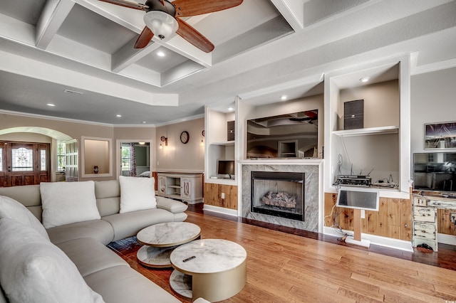living area featuring crown molding, wood finished floors, a high end fireplace, a ceiling fan, and coffered ceiling