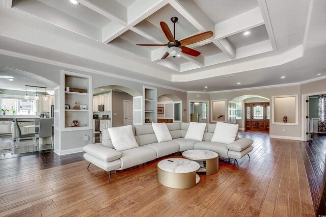 living area featuring ceiling fan, dark wood finished floors, ornamental molding, and coffered ceiling