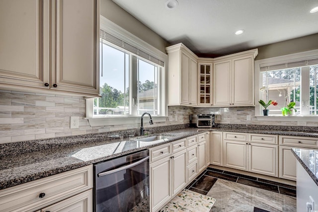 kitchen with a sink, dark stone countertops, backsplash, stainless steel dishwasher, and glass insert cabinets