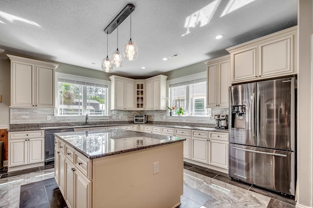 kitchen with dark stone counters, appliances with stainless steel finishes, a wealth of natural light, and cream cabinetry