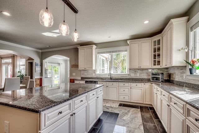 kitchen with crown molding, a kitchen island, recessed lighting, arched walkways, and backsplash