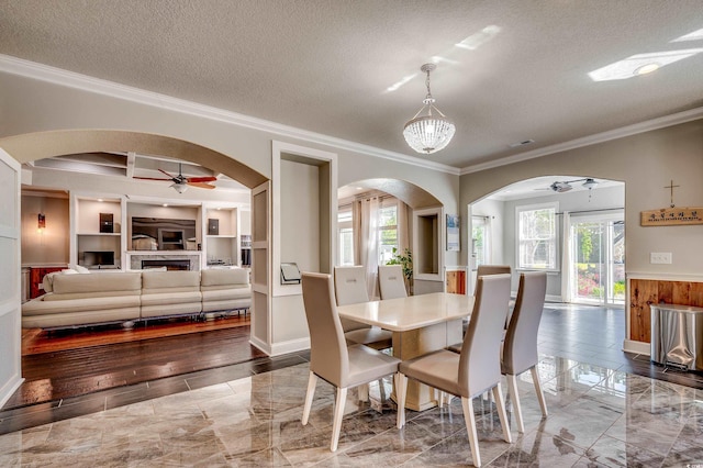 dining area featuring crown molding, arched walkways, a ceiling fan, and a textured ceiling