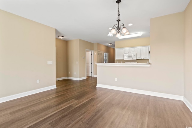 unfurnished living room featuring a chandelier, dark wood-style flooring, baseboards, and recessed lighting