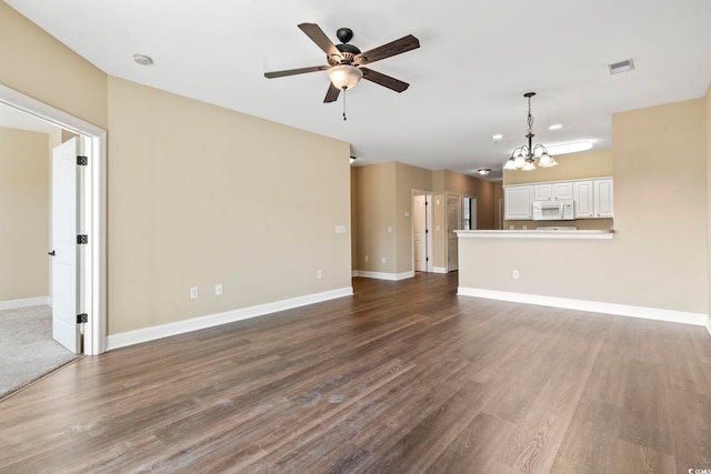 unfurnished living room featuring a ceiling fan, dark wood-style flooring, baseboards, and a chandelier