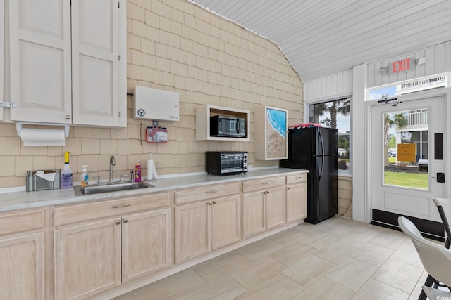 kitchen featuring a sink, black appliances, light brown cabinets, vaulted ceiling, and light countertops