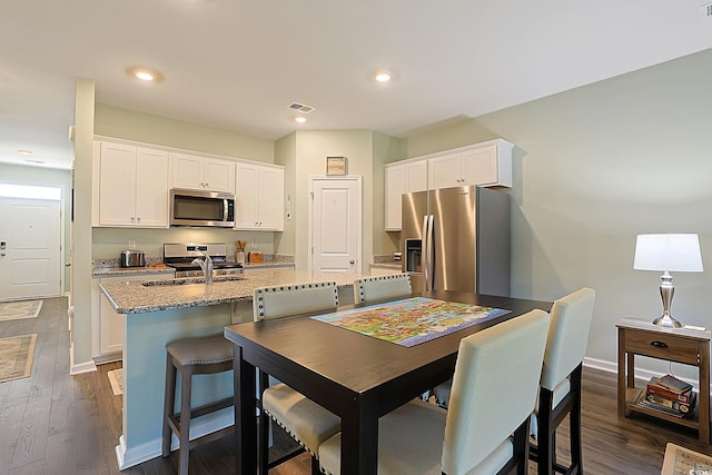 kitchen featuring dark wood-style flooring, appliances with stainless steel finishes, a center island with sink, and white cabinets