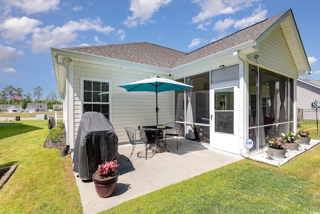 back of property featuring a yard, a patio, a shingled roof, and a sunroom