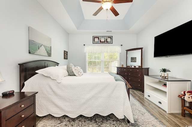 bedroom with a ceiling fan, visible vents, a raised ceiling, and light wood-style floors
