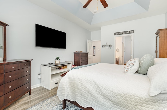 bedroom with connected bathroom, light wood finished floors, ceiling fan, and a tray ceiling