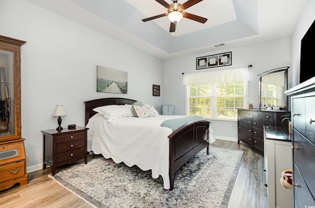 bedroom with visible vents, baseboards, a raised ceiling, and wood finished floors