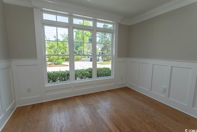 empty room featuring wood finished floors, wainscoting, crown molding, and a decorative wall