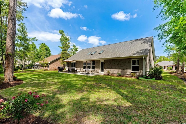 back of property with a lawn, roof with shingles, a patio, and brick siding