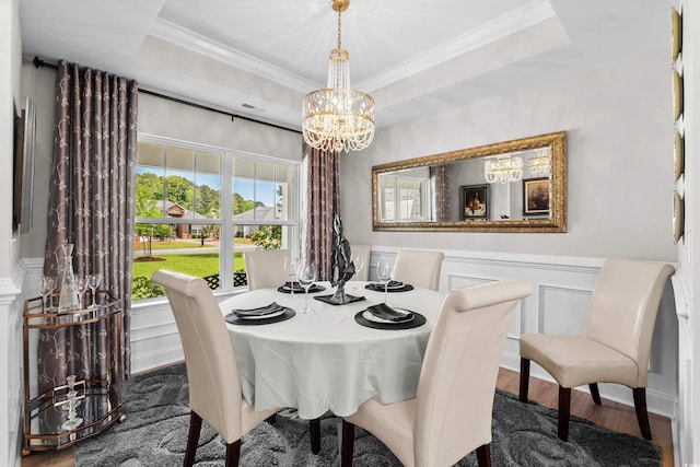 dining space featuring ornamental molding, an inviting chandelier, a decorative wall, a wainscoted wall, and wood finished floors