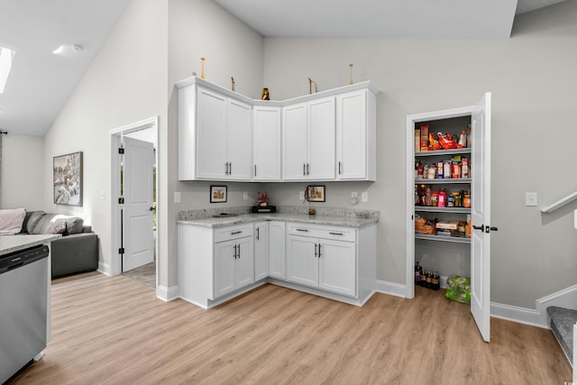kitchen with a skylight, white cabinets, stainless steel dishwasher, baseboards, and light wood-style floors