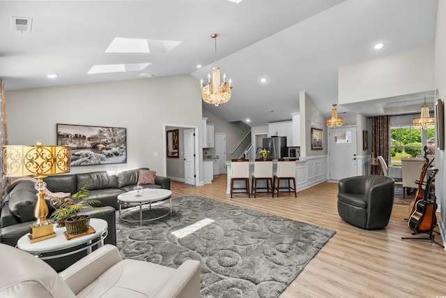 living area with high vaulted ceiling, light wood-style flooring, a skylight, and a notable chandelier