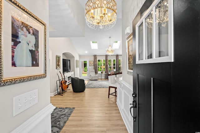 entryway featuring a high ceiling, a notable chandelier, arched walkways, and light wood-style floors