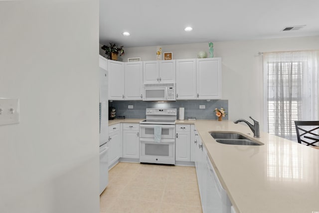 kitchen with tasteful backsplash, a sink, light countertops, white cabinets, and white appliances